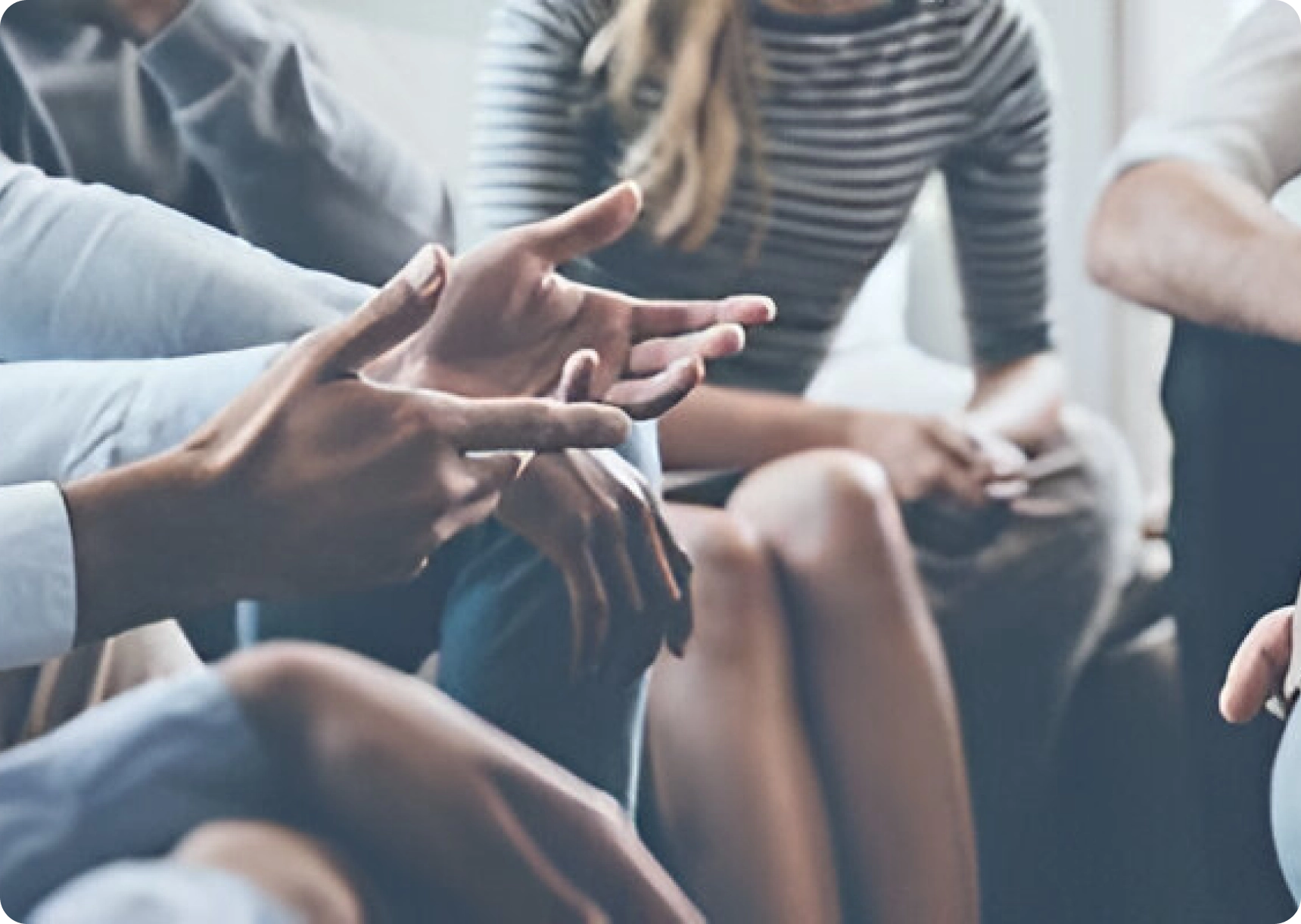 Close-up of a group discussion, showing gesturing hands and people seated closely, with one person wearing a striped shirt.